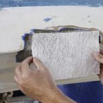 A worker is measuring a fiberglass sheet to repair a boat