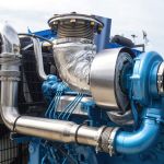Boat motor fragment. Engine with turbocharger. Ship blue engine close-up. Fragment of ships engine with propeller. Concept of maintenance and repair of ship motors. Huge open air boat motor