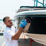 Boat maintenance - Man with orbital polisher polishing boat in marina.