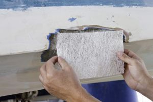 A worker is measuring a fiberglass sheet to repair a boat