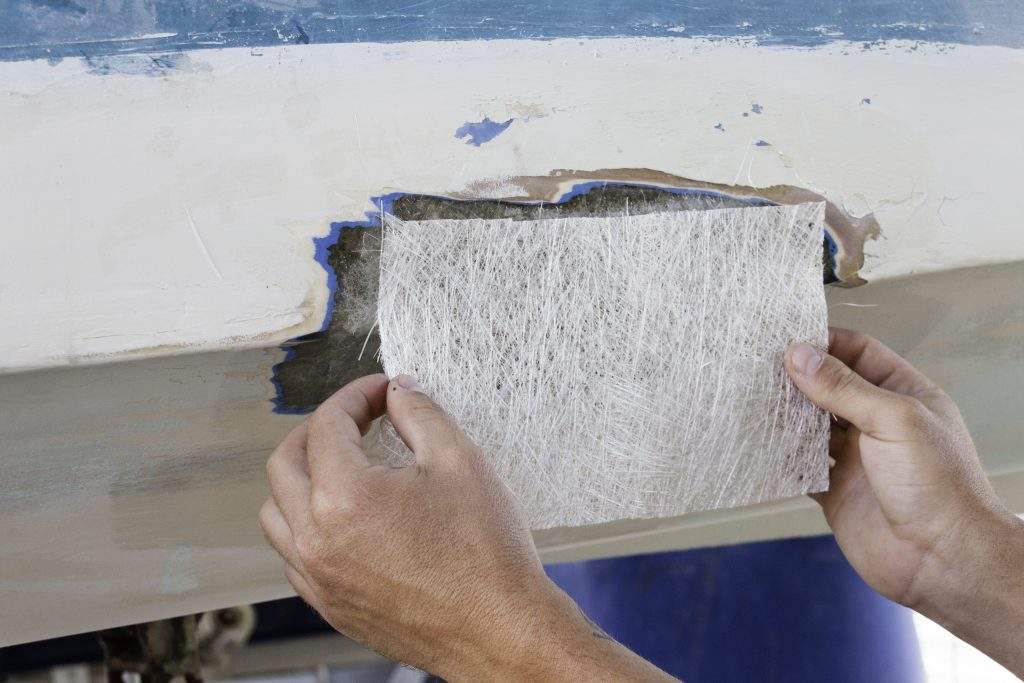 A worker is measuring a fiberglass sheet to repair a boat