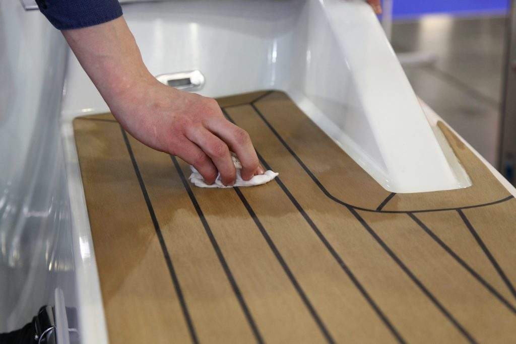 A man’s hand rubs oil on marine teak on the deck of a white moto