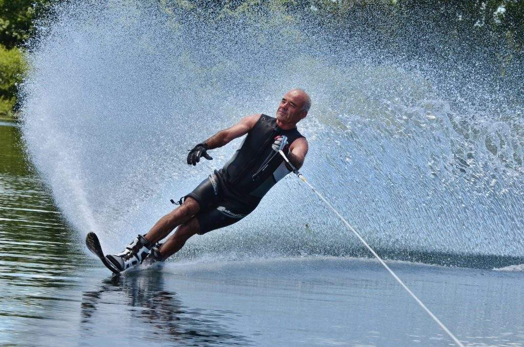 A water skier in his 60's preforming water skiing sport on a lake.